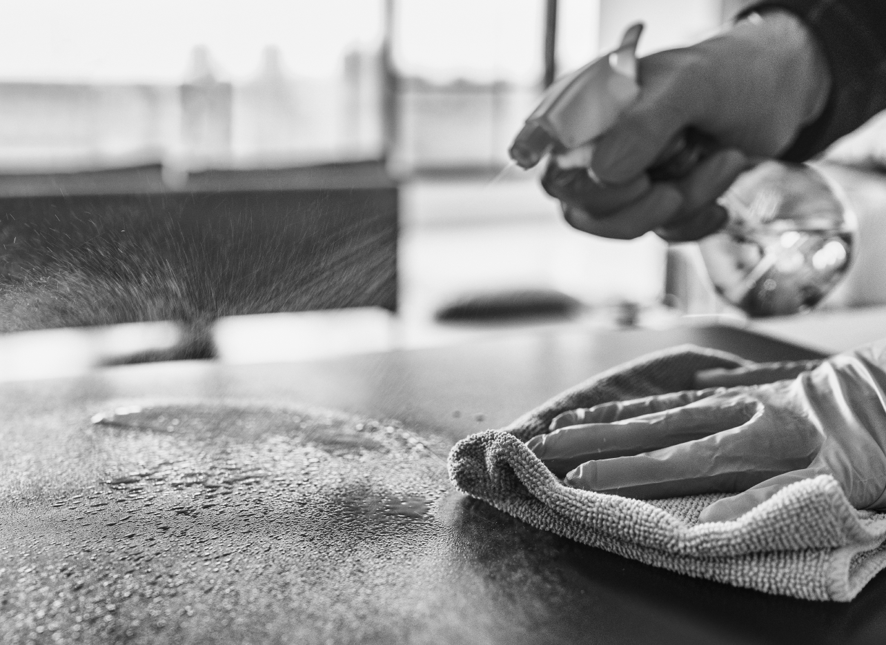 person cleaning a table with spray bottle and cloth